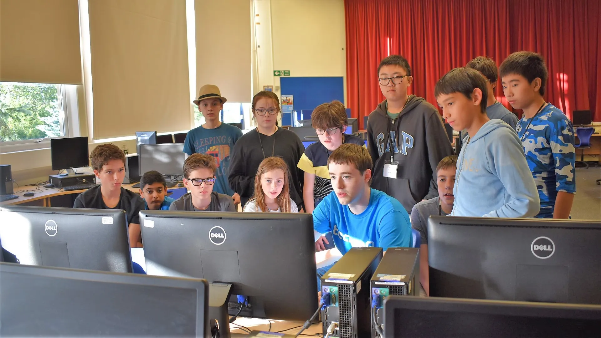 Students grouped around tutor demonstrating something on a computer screen at Tech Camp