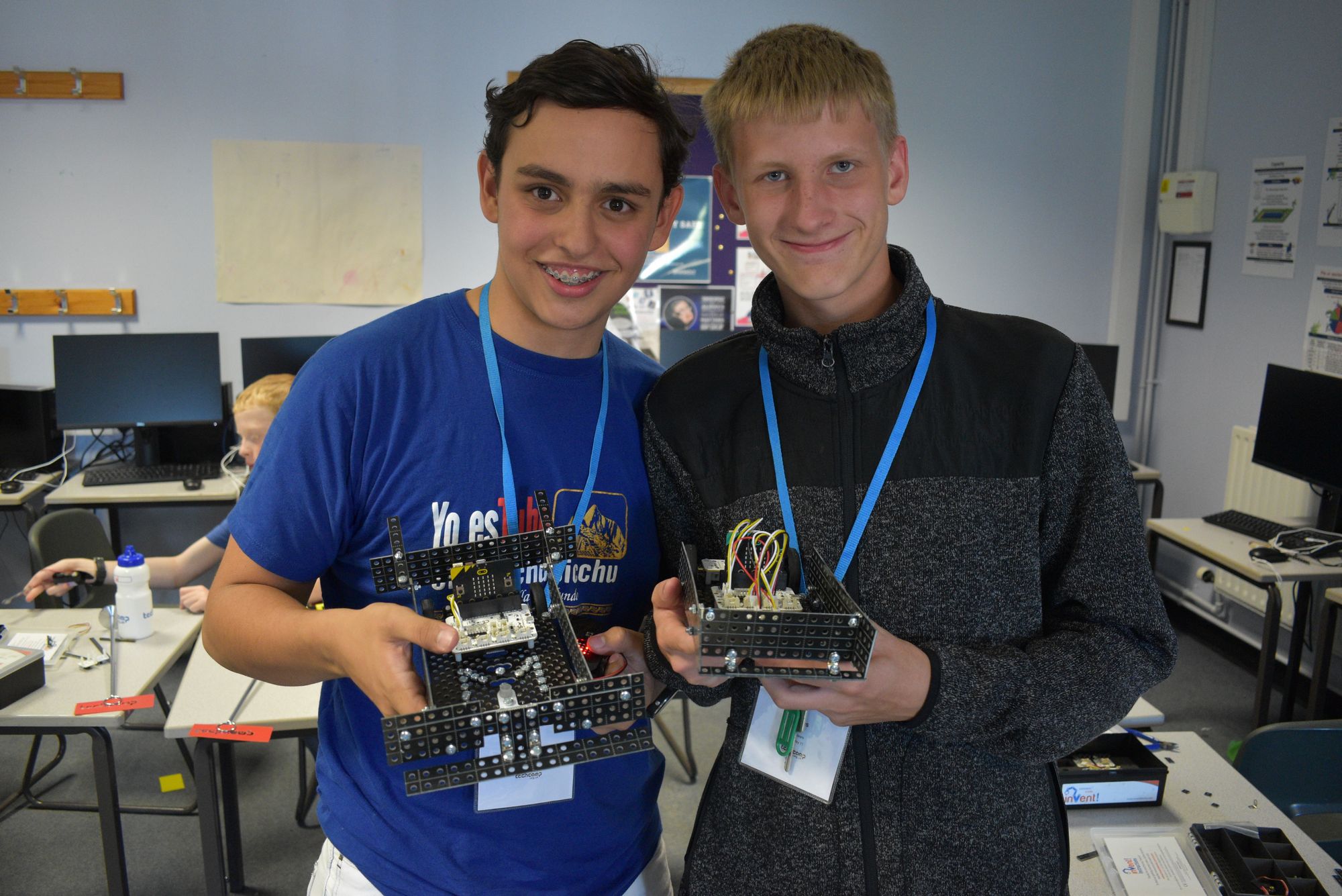 Two teen boys at Tech Camp holding up their custom robots